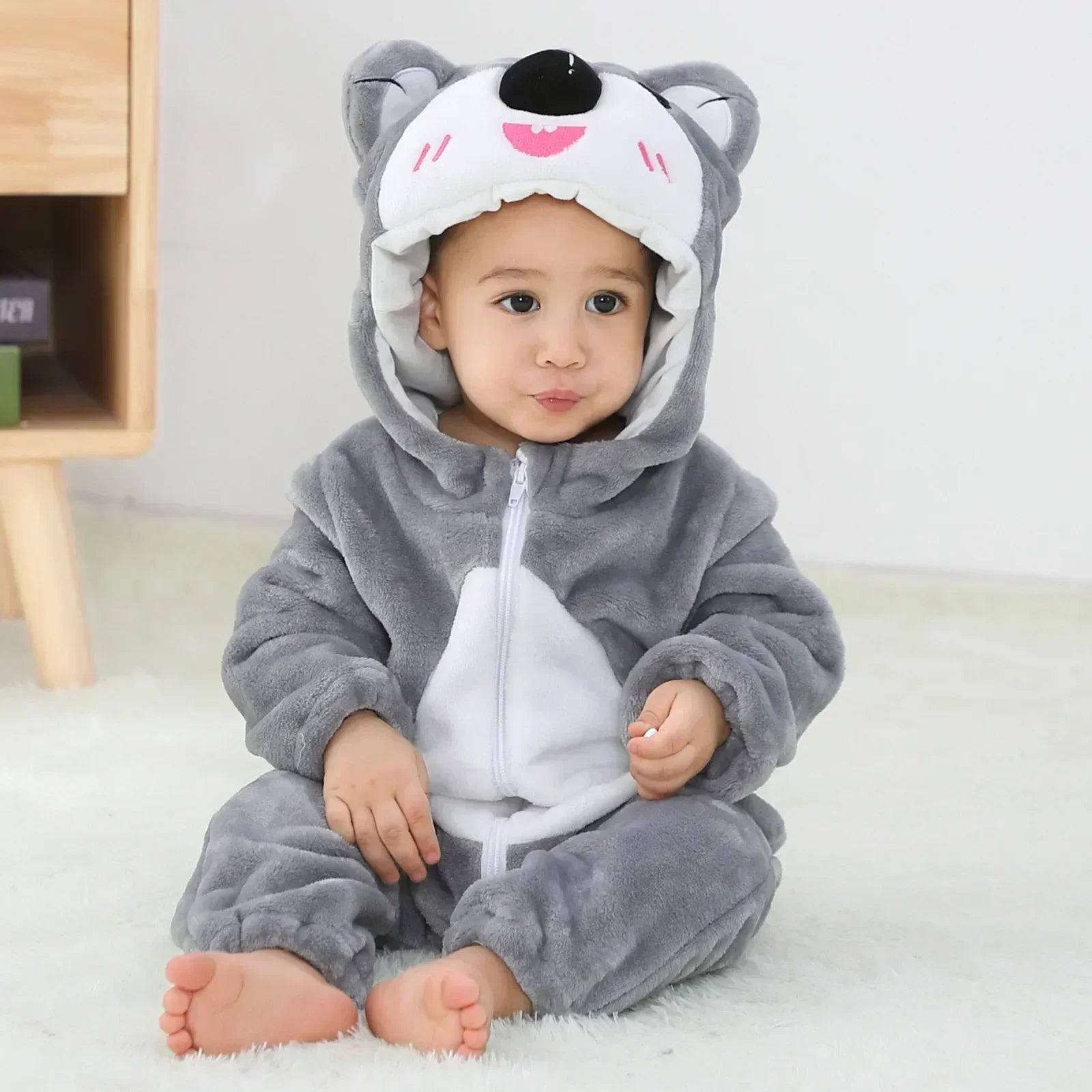 Child wearing a gray and white animal onesie with a hood on a light background